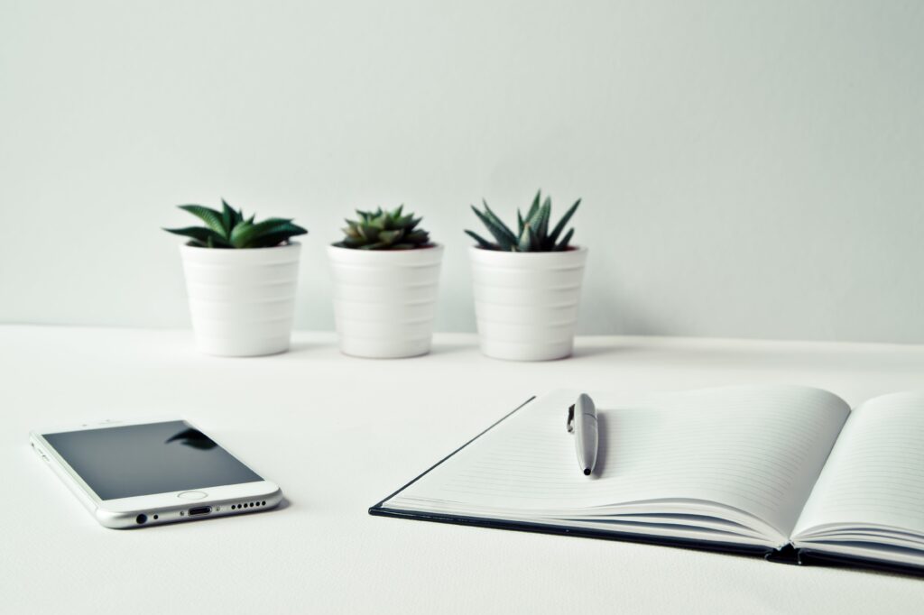 Uninspiring white room with white desk, cell phone, notebook, and potted plants echoes Stanford's changing culture.