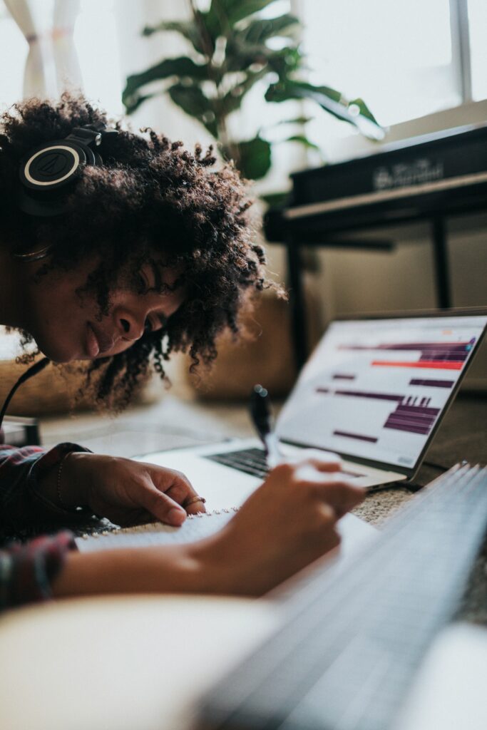 Young woman writes in a notebook with a laptop open in front of her and headphones on her head. Building your ideal study abroad experience involves learning the language.