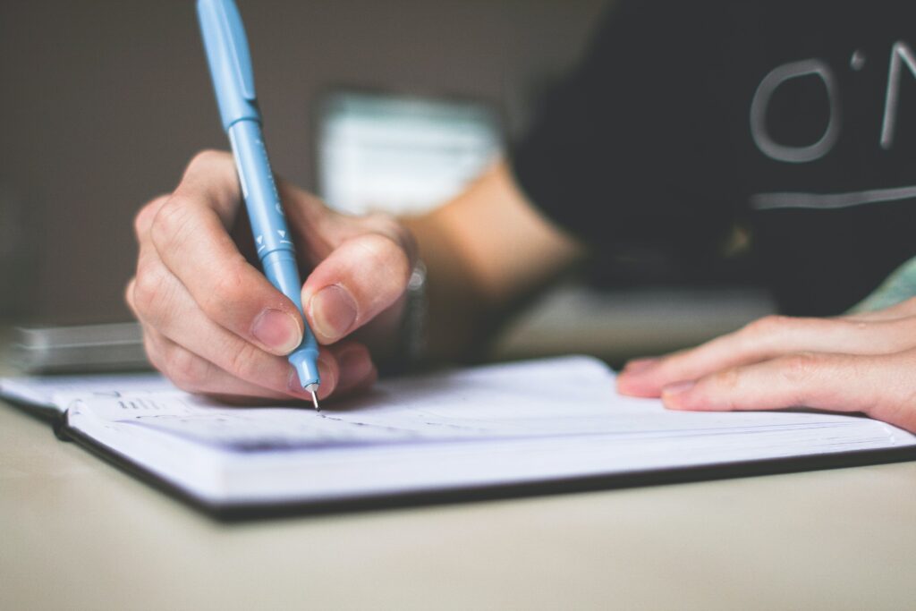 A hand uses a pen to write in a journal. Frequently writing with AI means you'll feel intimidated by writing long term.